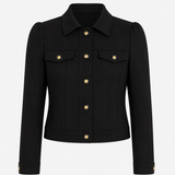 A black cropped jacket with structured shoulders, a pointed collar, flap chest pockets, and gold-tone buttons, shown on a plain light gray background.