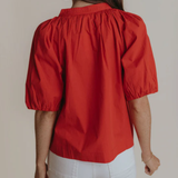 Person wearing a red blouse with puff sleeves against a neutral background