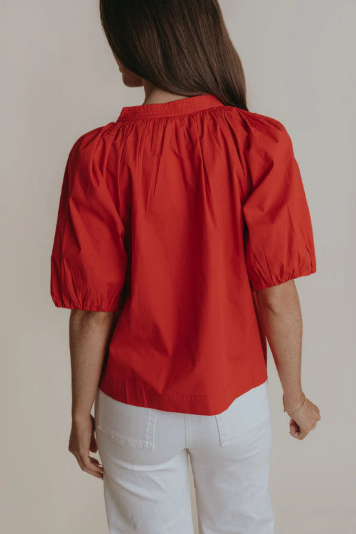 Person wearing a red blouse with puff sleeves against a neutral background