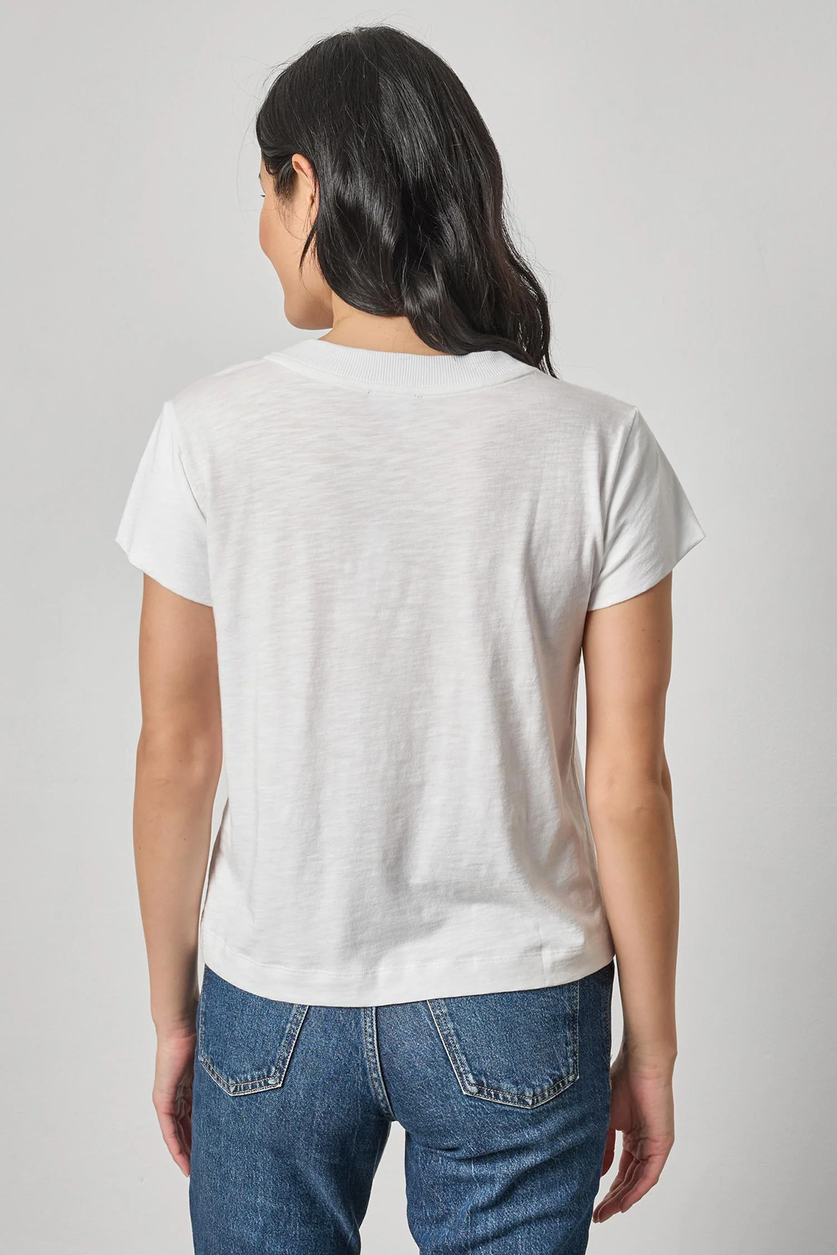 Person wearing a plain white t-shirt and blue jeans on a light gray background