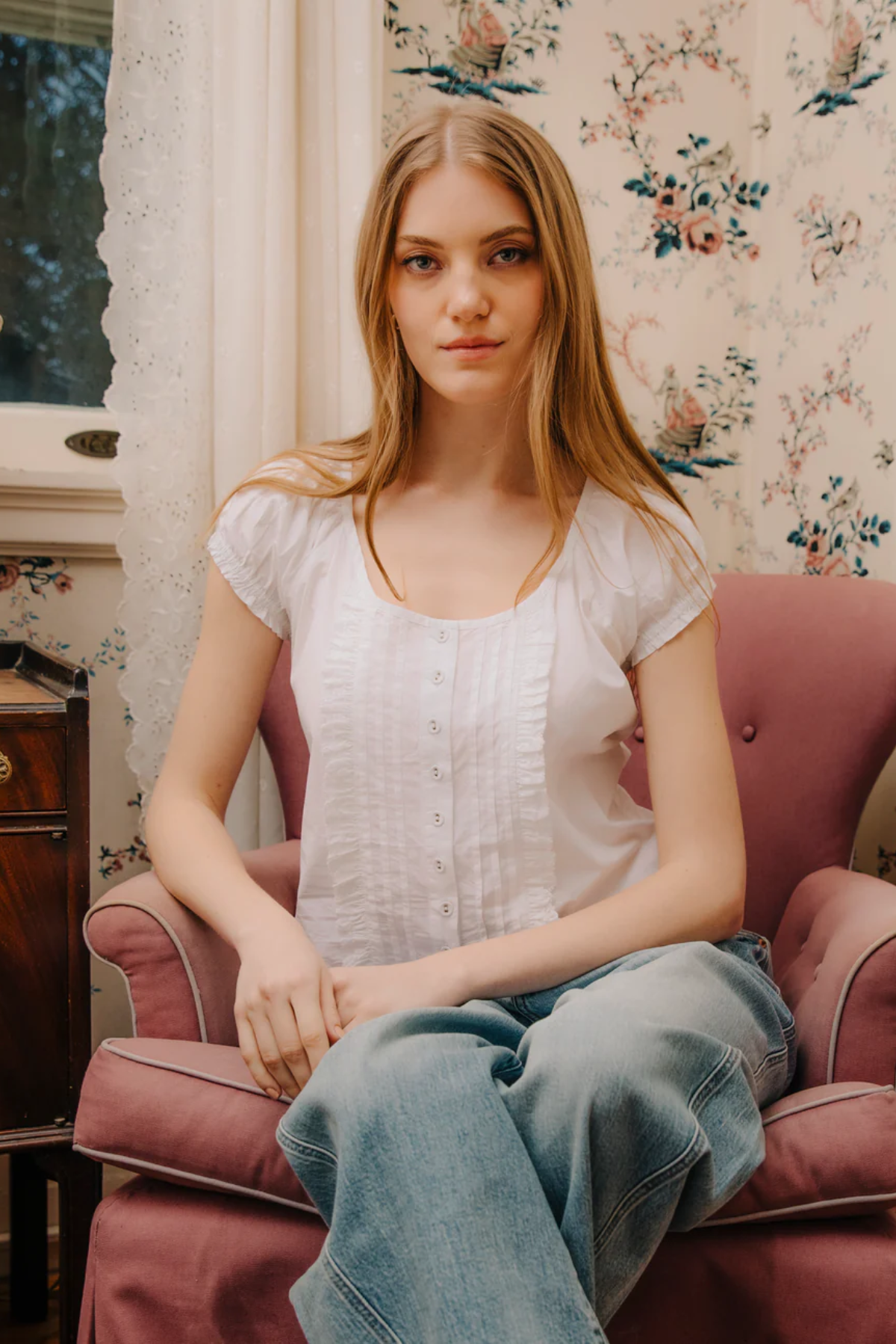 Woman sitting on a pink armchair in a room with floral wallpaper