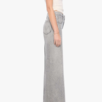A side-profile view of a model wearing light gray wide-leg denim jeans, a cream ribbed tank top, and black pointed-toe heels against a plain white background.