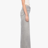 A side-profile view of a model wearing light gray wide-leg denim jeans, a cream ribbed tank top, and black pointed-toe heels against a plain white background.