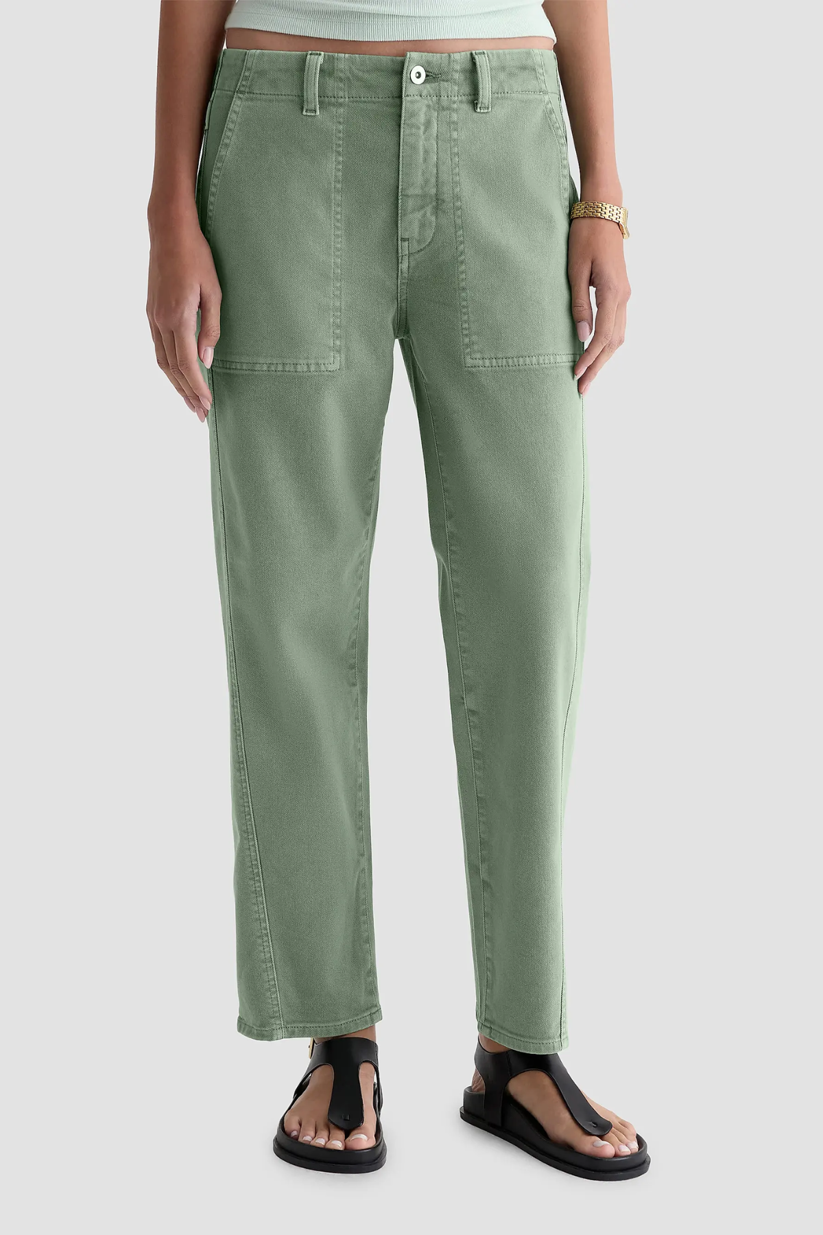 A person wearing sage green straight-leg pants with front patch pockets, shown from the waist down against a light gray studio background.