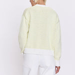 Person wearing a light green and white striped sweater with white pants on a white background