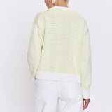 Person wearing a light green and white striped sweater with white pants on a white background