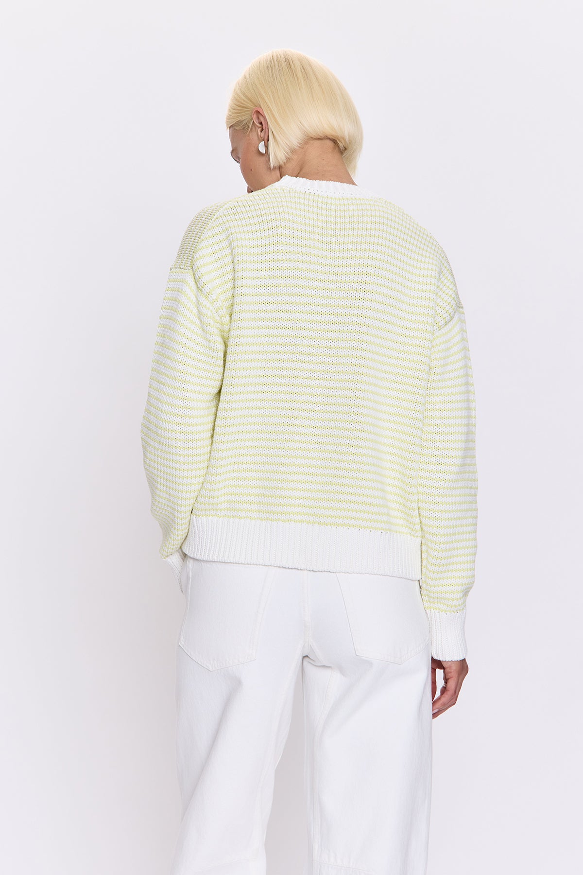 Person wearing a light green and white striped sweater with white pants on a white background