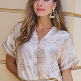Woman wearing a white patterned outfit with gold earrings against a neutral background