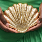Gold shell-shaped clutch held by hands against a green fabric background