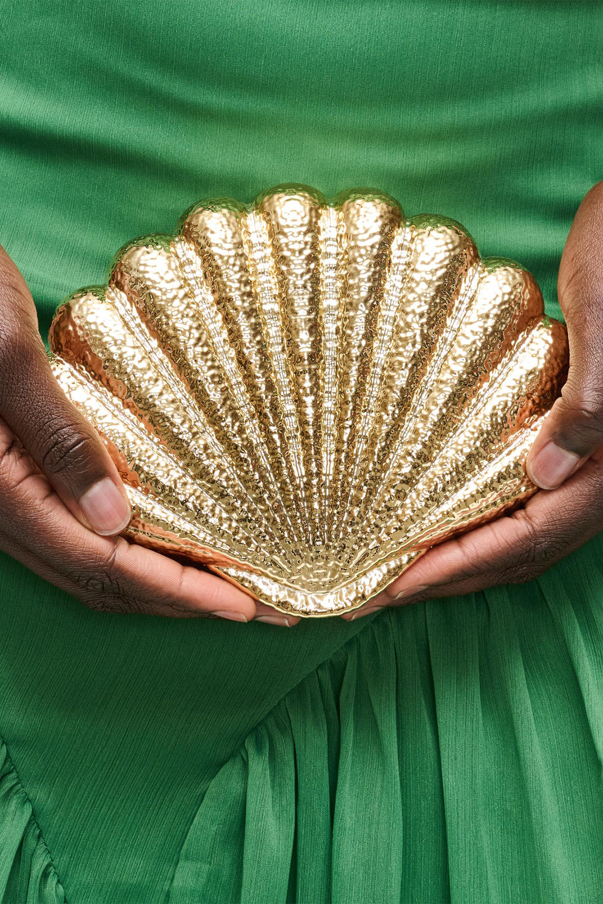 Gold shell-shaped clutch held by hands against a green fabric background