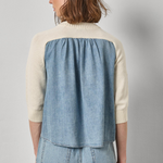 Woman wearing a two-tone jacket with beige and denim sections on a gray background