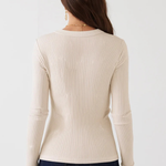 A woman viewed from the back wearing a cream ribbed long-sleeve sweater and dark blue jeans against a plain white background.
