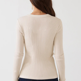 A woman viewed from the back wearing a cream ribbed long-sleeve sweater and dark blue jeans against a plain white background.