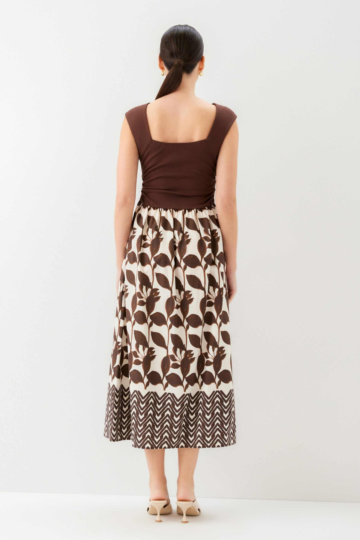 Woman wearing a brown top and patterned skirt on a white background