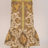 A long skirt with a ruffled hem, featuring a vertical olive green stripe down the center flanked by symmetrical paisley patterns in brown, gold, and beige. The skirt is shown on a model wearing tan pointed-toe heels against a plain light gray background.