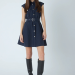 A woman modeling a sleeveless navy blue pinstriped mini dress with a matching belt and silver buckle, paired with black knee-high boots against a light gray studio background.