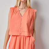 Woman wearing a coral sleeveless top and skirt set against a plain background