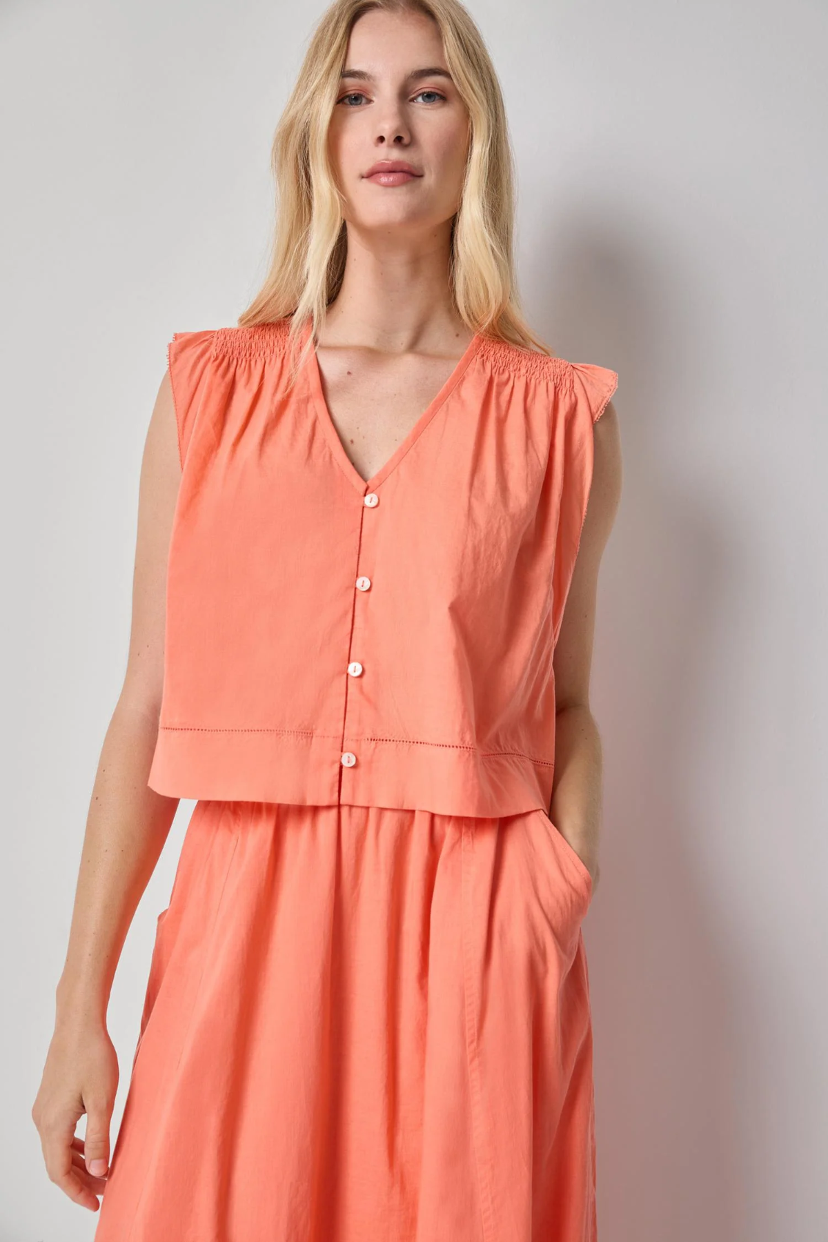 Woman wearing a coral sleeveless top and skirt set against a plain background