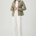 Woman wearing a green jacket, white top, and white pants on a light gray background