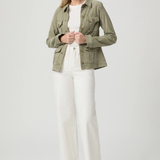 Woman wearing a green jacket, white top, and white pants on a light gray background
