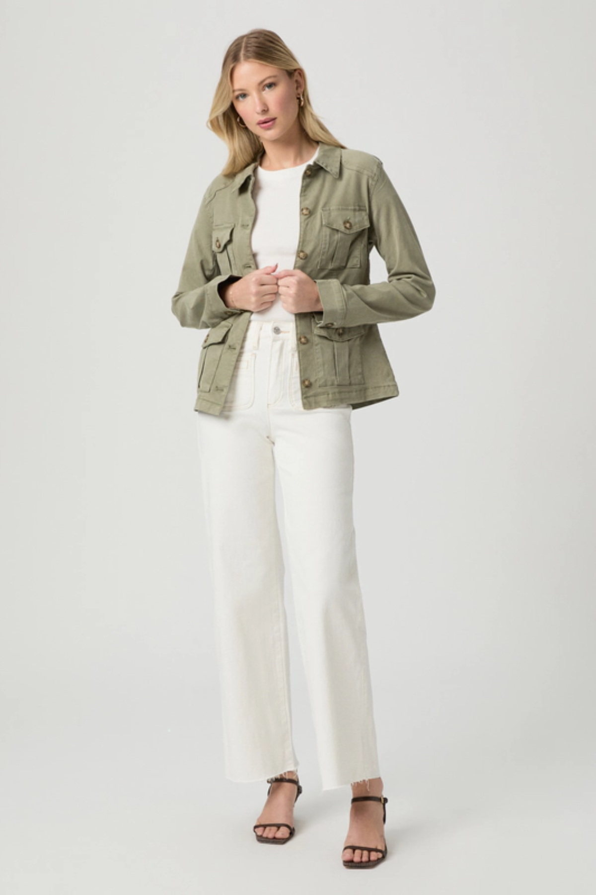 Woman wearing a green jacket, white top, and white pants on a light gray background