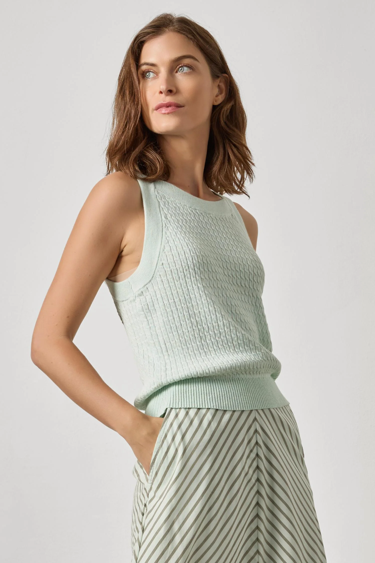 Woman wearing a light green sleeveless knitted top against a plain background