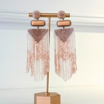 A pair of rose gold beaded tassel earrings displayed on a matching rose gold stand against a white background.