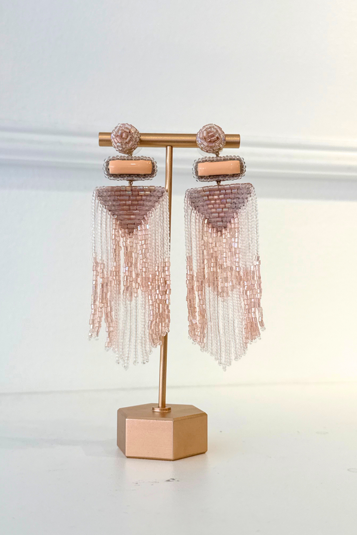 A pair of rose gold beaded tassel earrings displayed on a matching rose gold stand against a white background.