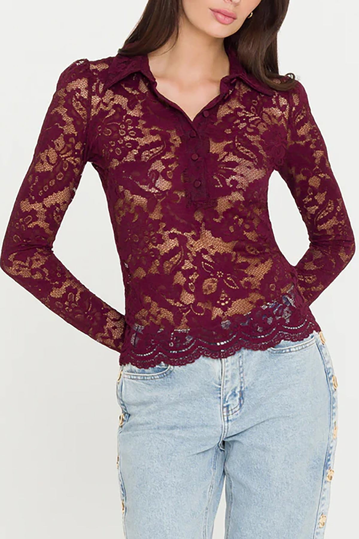 Woman wearing a burgundy lace top and light blue jeans on a white background