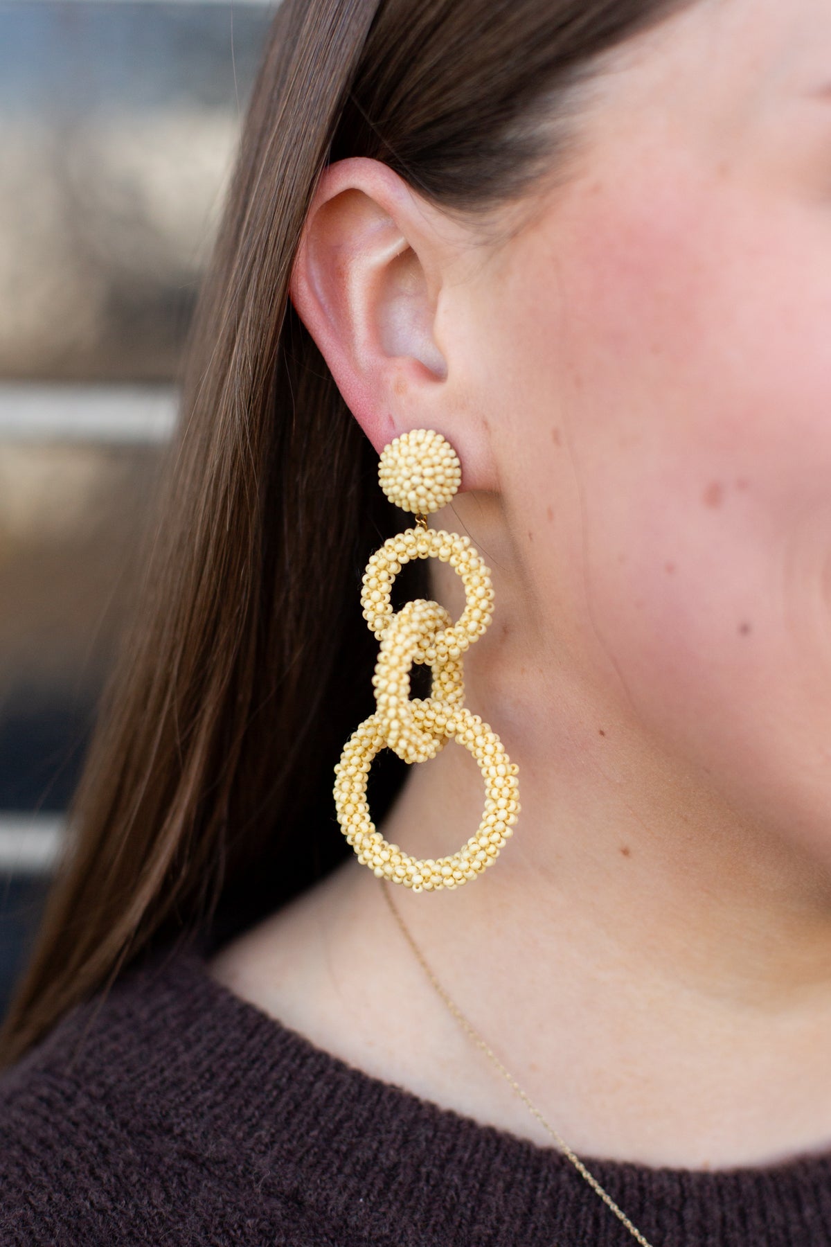 Close-up of a person wearing gold hoop earrings with a blurred background