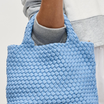 Blue woven handbag held by a person wearing a gray sweatshirt.