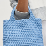 Blue woven handbag held by a person wearing a gray sweatshirt.
