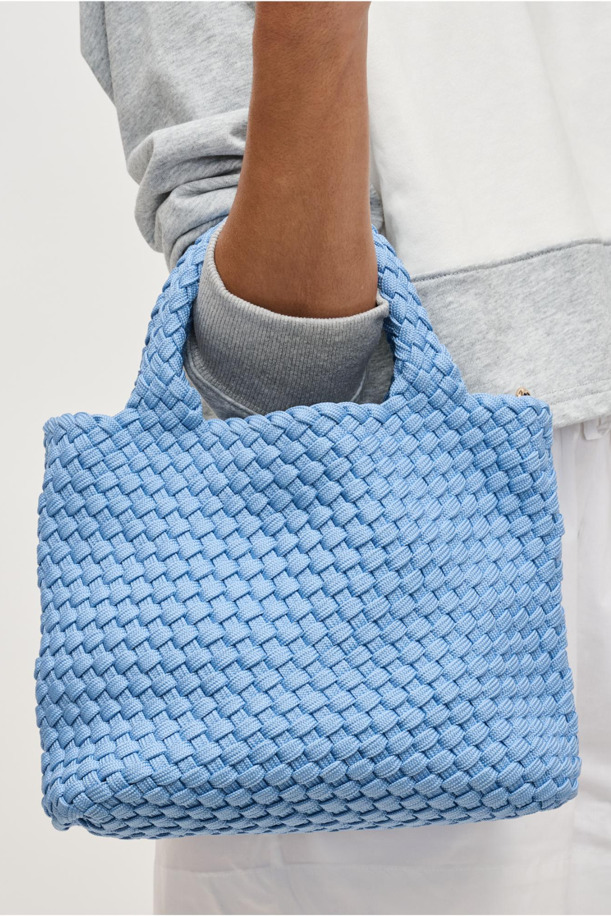 Blue woven handbag held by a person wearing a gray sweatshirt.