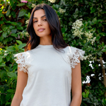 ivory tee with lace details worn by a model with pink pants against greenery