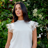 ivory tee with lace details worn by a model with pink pants against greenery