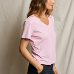 Woman wearing a light pink shirt and dark pants against a plain background
