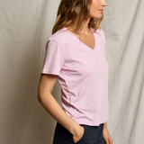 Woman wearing a light pink shirt and dark pants against a plain background