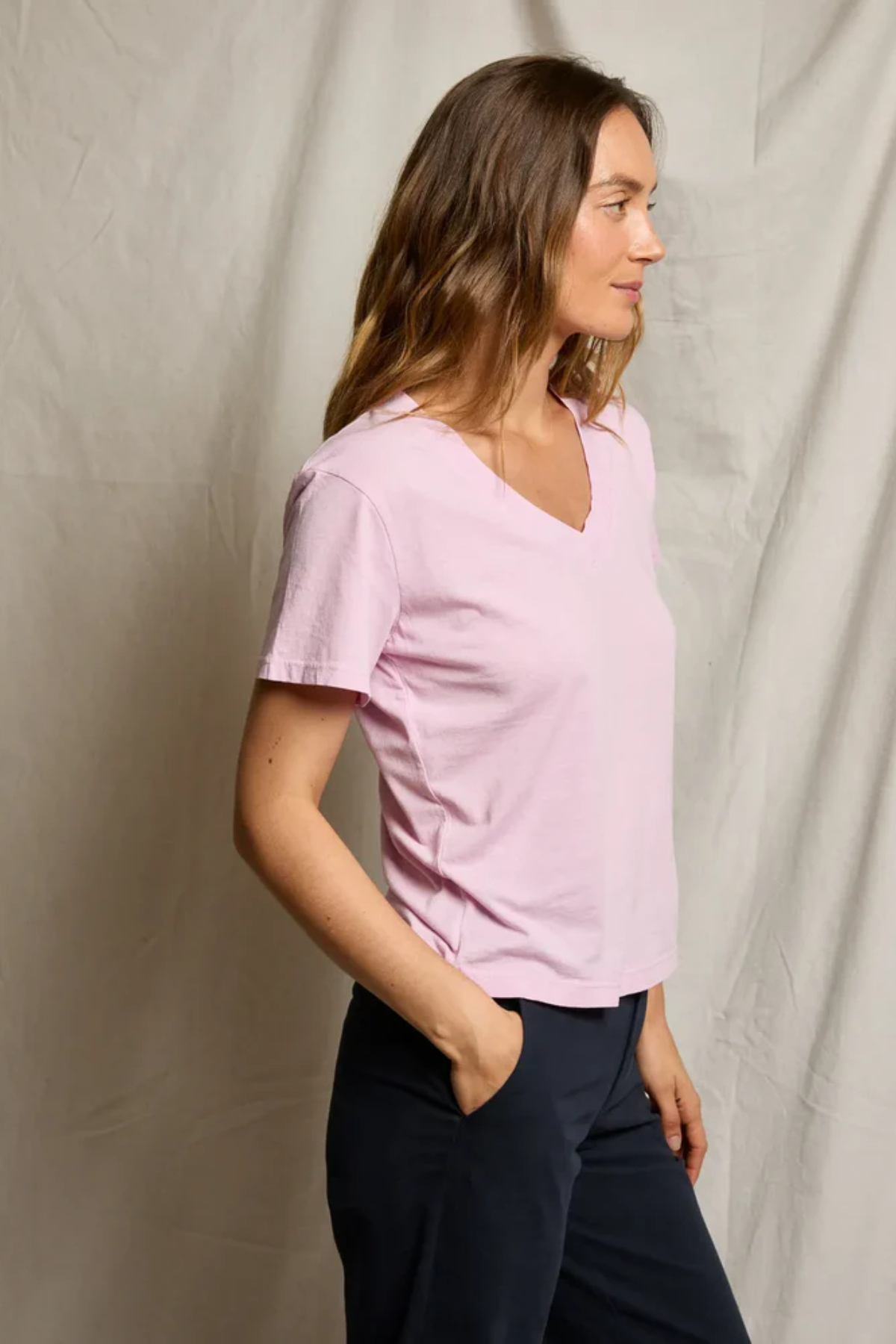 Woman wearing a light pink shirt and dark pants against a plain background