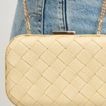 Beige quilted handbag with gold chain strap held by a person wearing blue jeans.