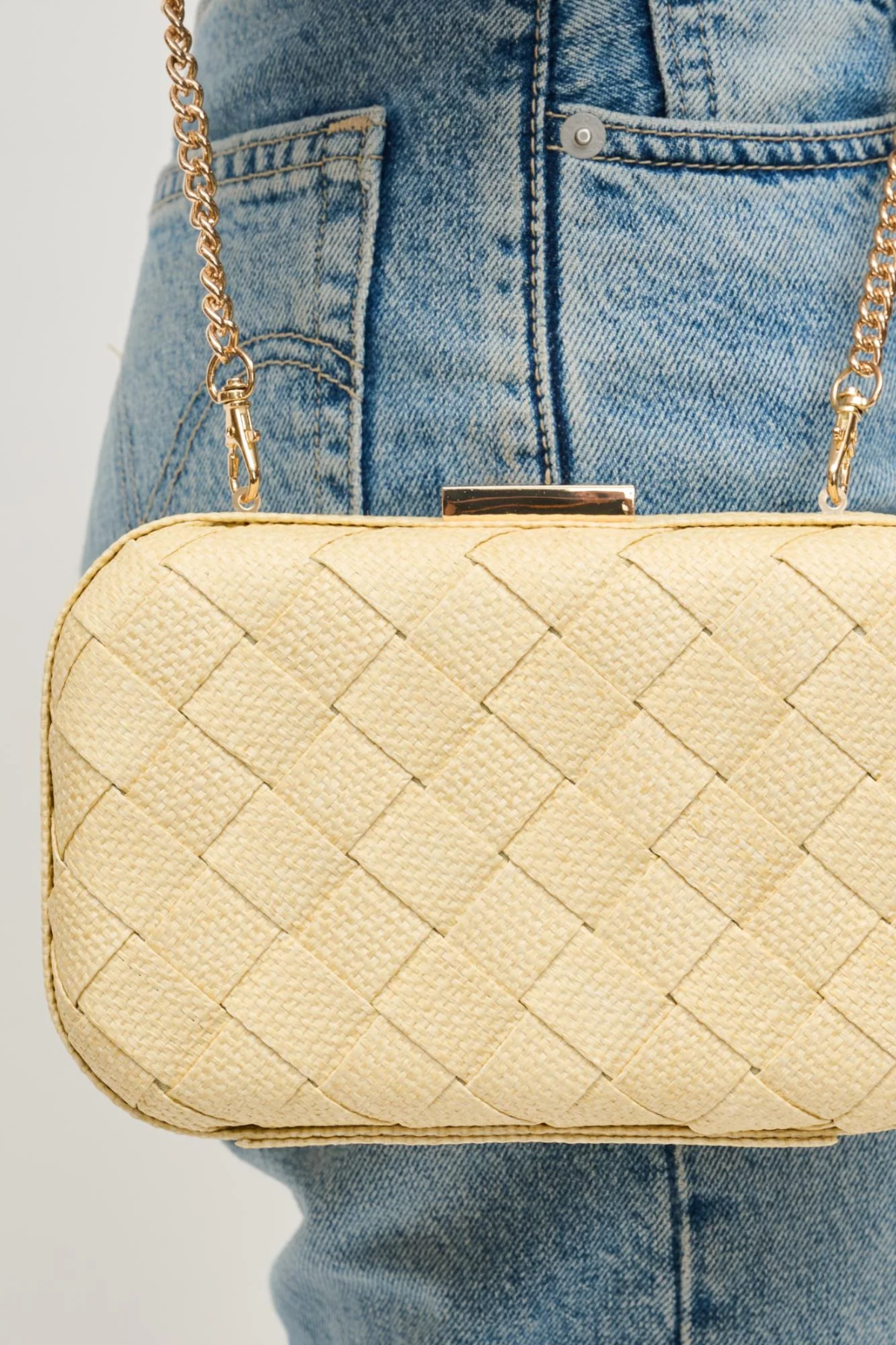 Beige quilted handbag with gold chain strap held by a person wearing blue jeans.