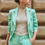 Woman wearing a mint green suit standing against a stone wall.