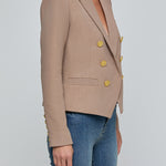 Beige blazer with gold buttons worn by a person on a light gray background