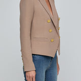 Beige blazer with gold buttons worn by a person on a light gray background