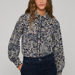 A woman modeling a long-sleeve button-up shirt with a navy blue and gray botanical pattern, paired with dark navy jeans, against a solid light gray background.