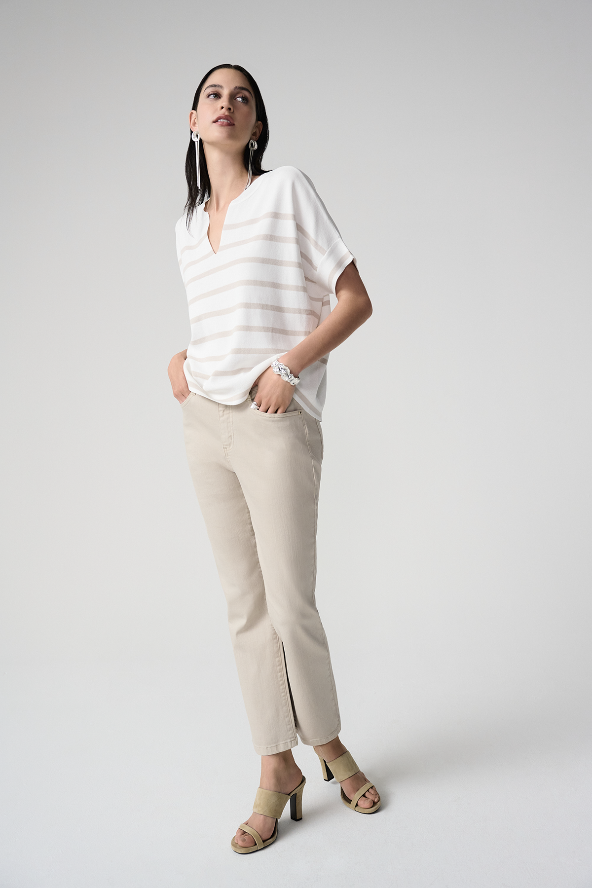 Woman wearing a white striped shirt and beige pants on a plain background