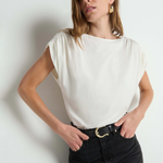 Woman wearing a white top and black pants against a plain background