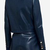 A model shown from the back wearing a dark navy faux-leather cropped jacket and matching shorts, featuring gold button details on the cuffs.