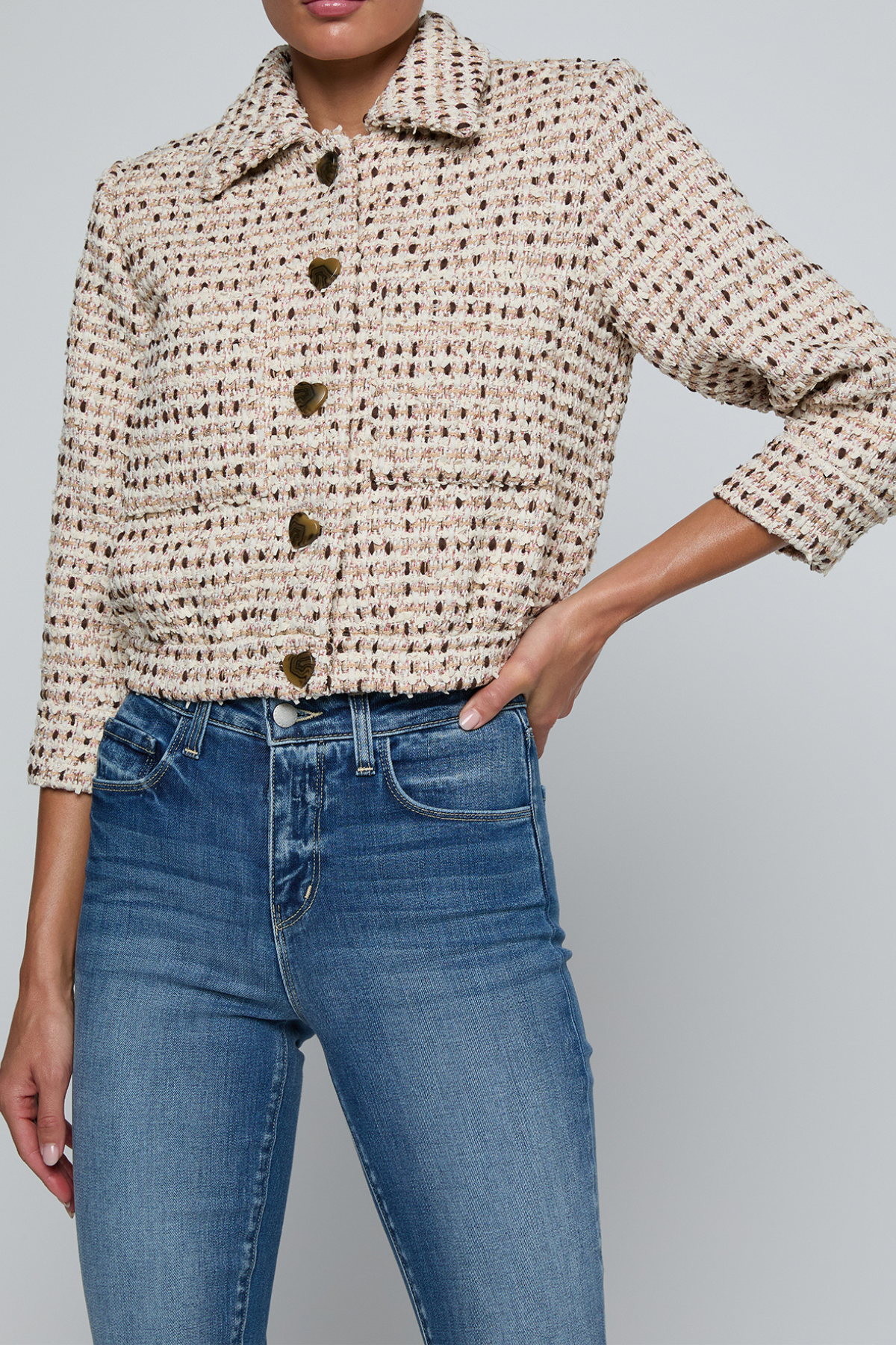 Model wearing a tweed jacket with jeans on and off white background.
