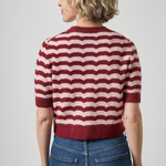 A woman shown from the back wearing a short-sleeve knit sweater with horizontal wavy stripes in burgundy and cream, paired with blue jeans, against a light gray studio background.