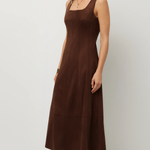 A woman modeling a sleeveless brown midi dress with a square neckline and side pockets, paired with snakeskin-patterned boots, against a plain light gray studio background.
